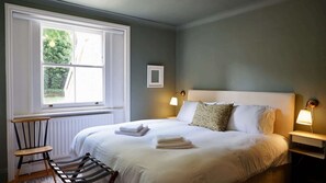 Ein Schlafzimmer mit großem Fenster, einem Bett mit weißer Bettwäsche, zwei Nachttischlampen und einem kleinen Tisch mit Stuhl.