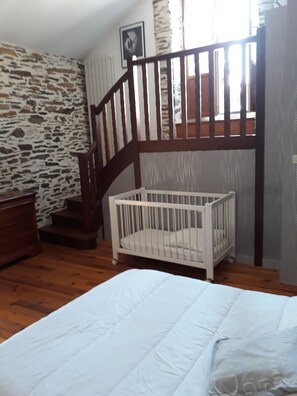 Ein Zimmer mit einer Holztreppe, einem weißen Babybett und einem Bett.