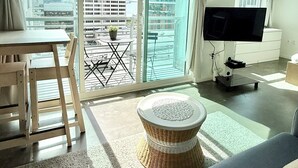 En moderne stue med sofa, fjernsyn, spisebord og en balkon med udsigt over byen.