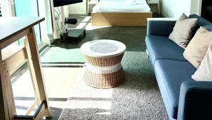 Et hotelværelse med seng, sofa, fjernsyn, skrivebord og et vindue med gardiner.