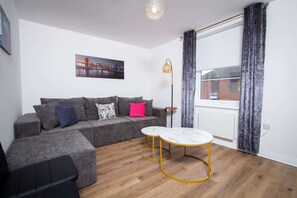 Ein modernes Wohnzimmer mit Ecksofa, einem kleinen runden Tisch und einer Stehlampe.