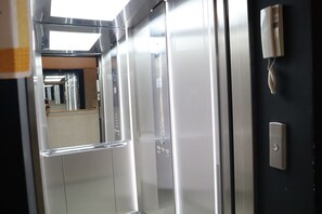 Innenansicht eines Aufzugs mit Metallwänden, einer Handlauf und einem an der Wand montierten Telefon.