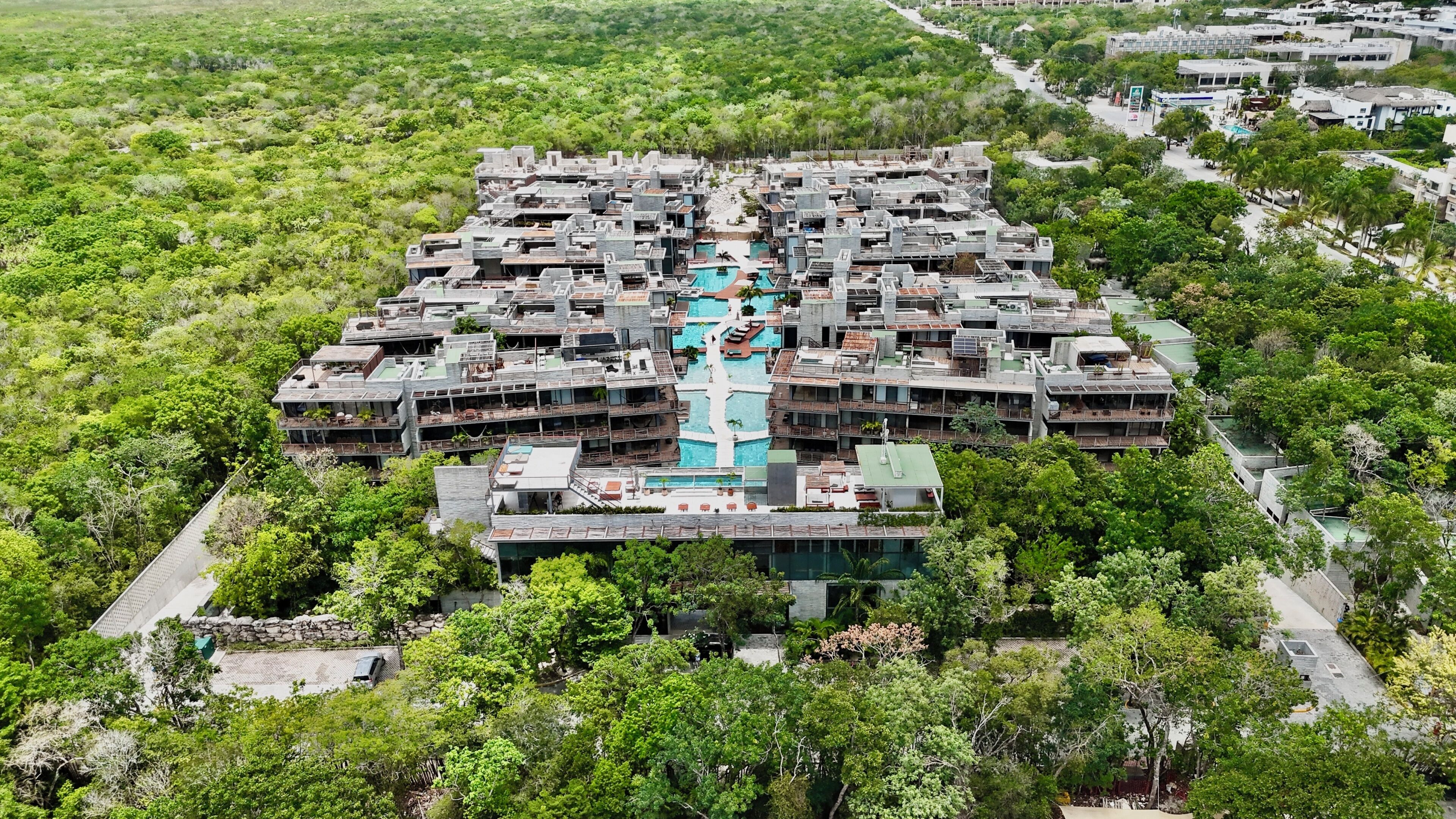 Ein großes Hotel mit mehreren Etagen, einem zentral gelegenen Pool und umgeben von dichter Vegetation.