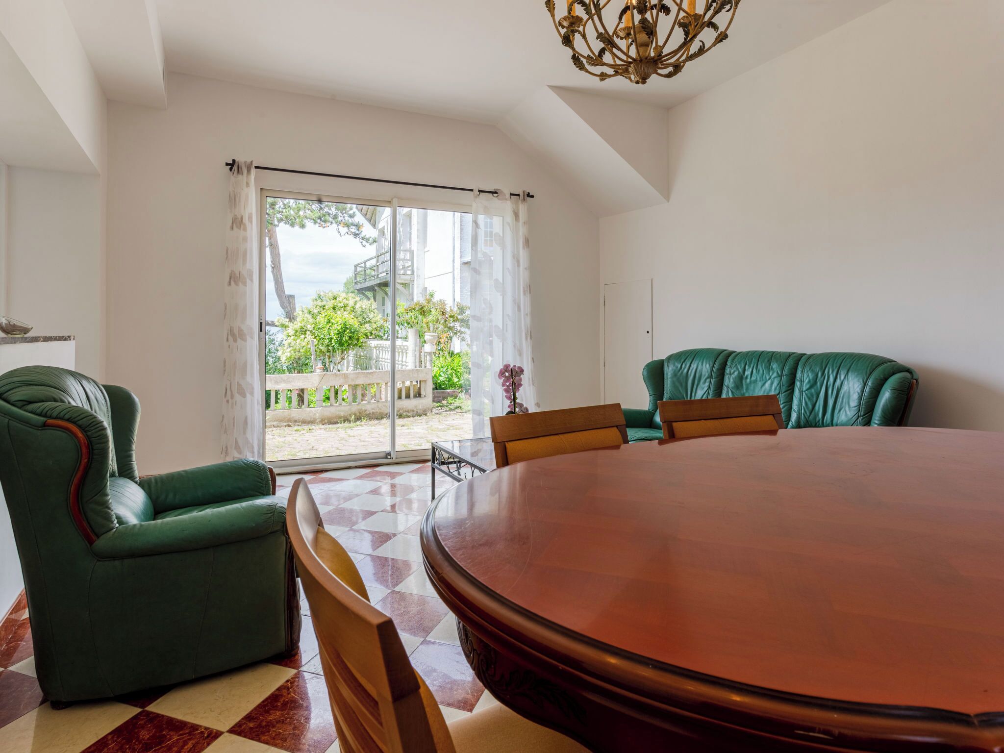 Quarto com uma mesa redonda grande, cadeiras de couro verde, um sofá verde e vista através de uma porta de vidro.