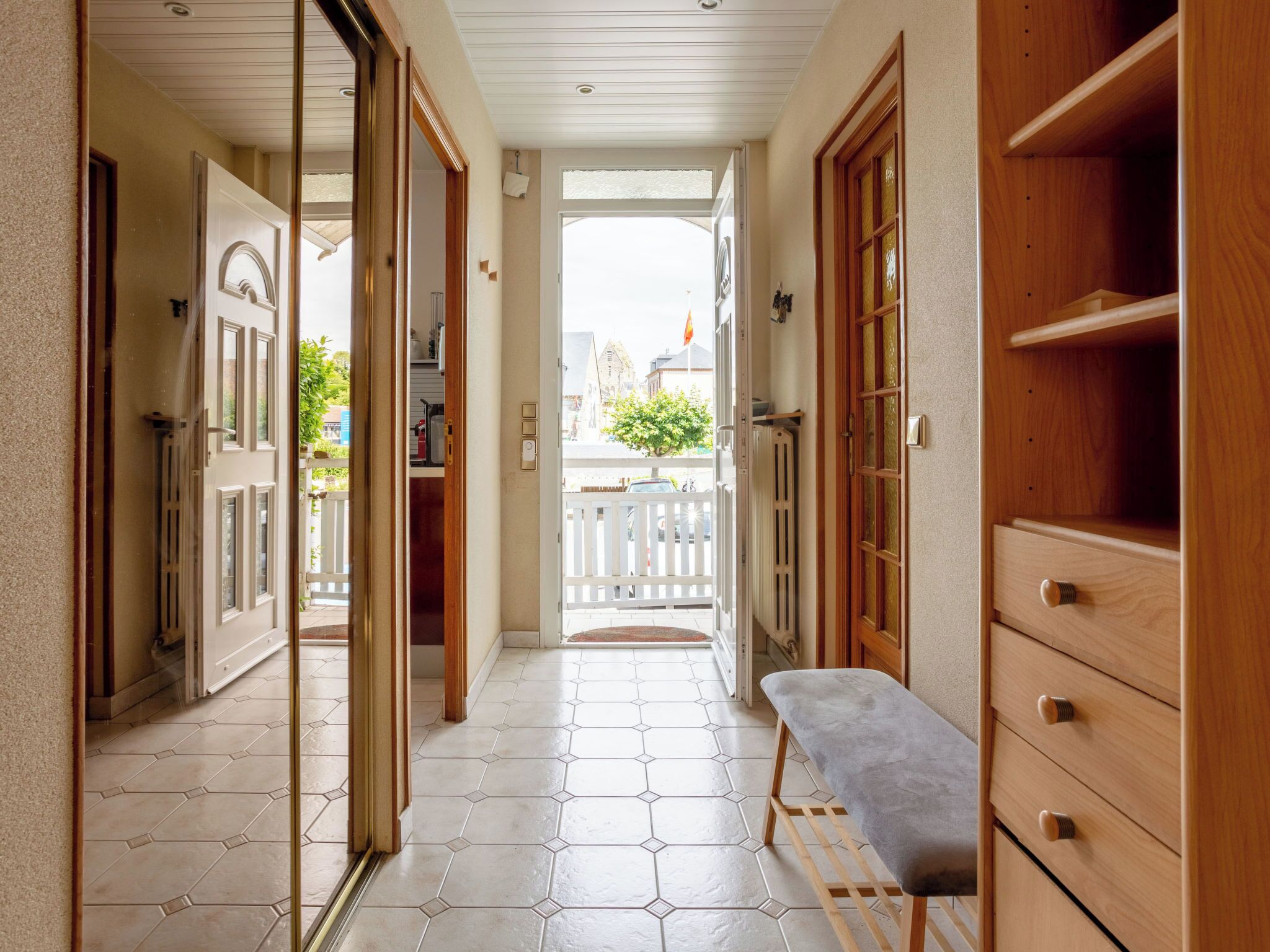 A hallway with a bench, wooden cabinets, and a view to the outside.