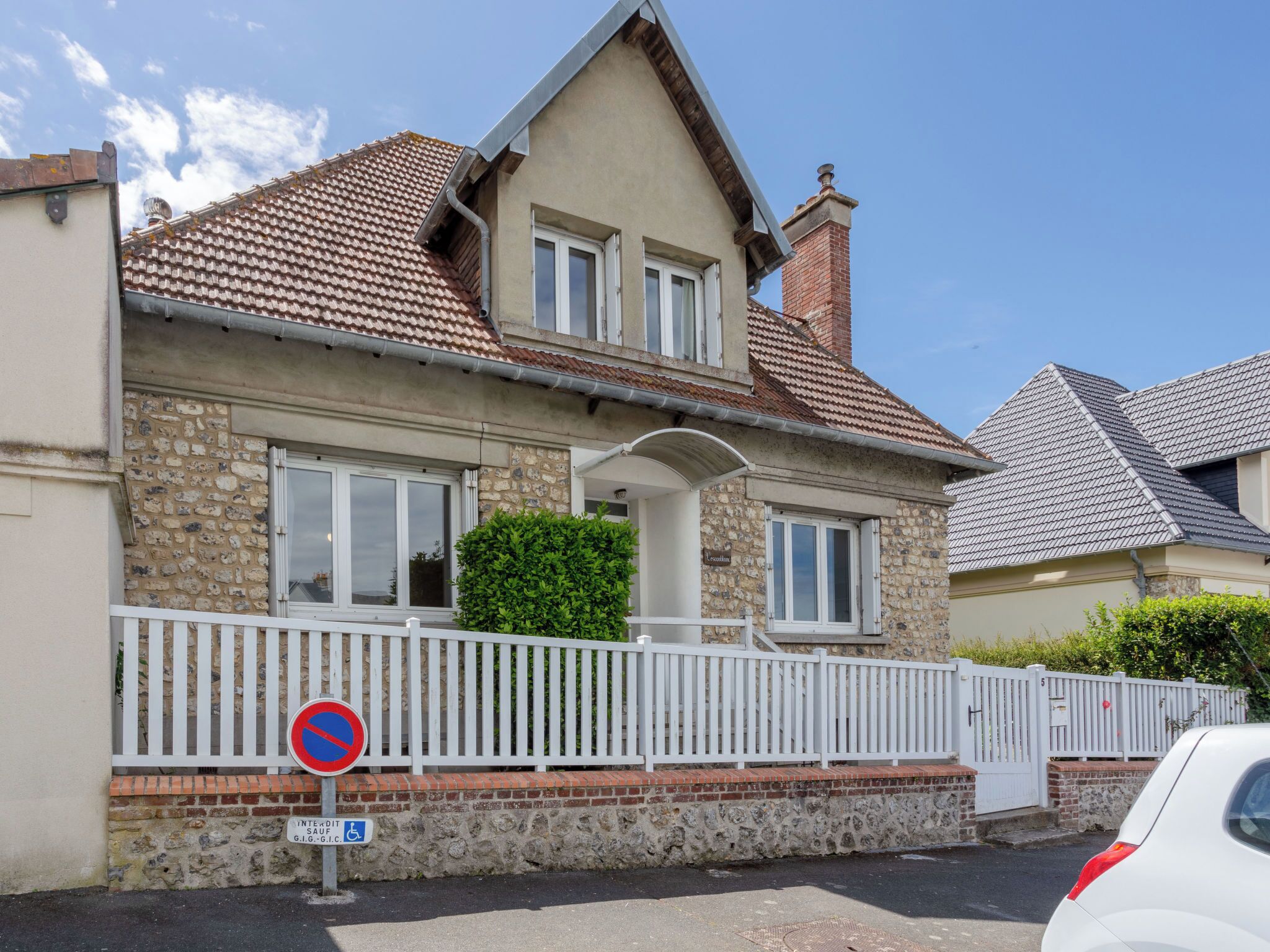 A two-story house with a stone facade, a tiled roof, and a white fence.