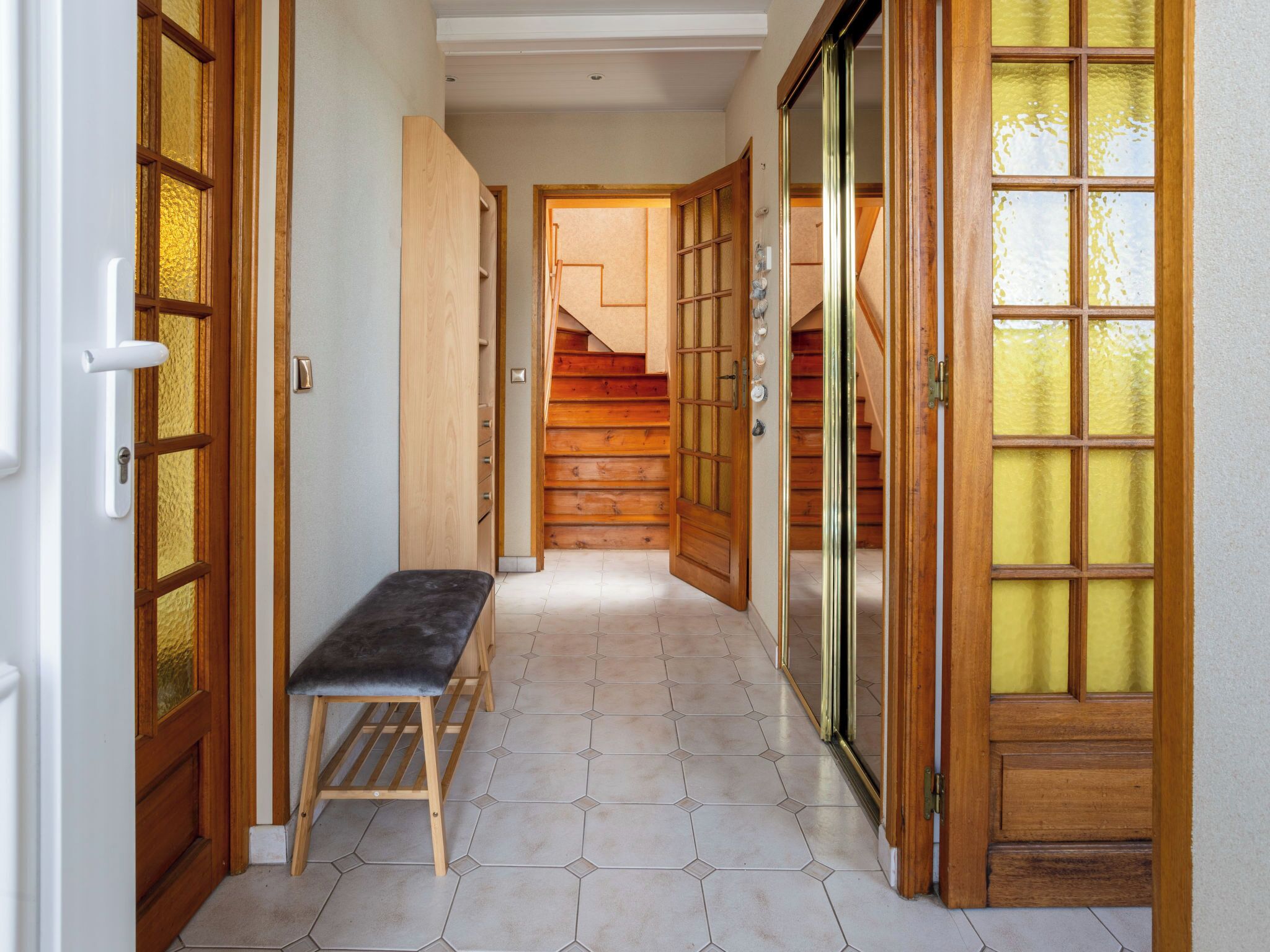 A hallway with a bench, wooden doors, and a staircase.