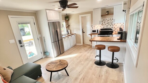 Eine moderne Küche mit Kühlschrank, Mikrowelle und Herd, ein Essbereich mit Hockern, einem Deckenventilator und Blick durch eine Tür.