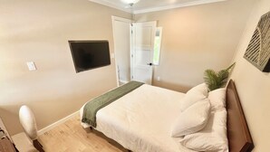Ein Schlafzimmer mit einem Bett, einem Fernseher an der Wand, einer Tür und einer Pflanze.