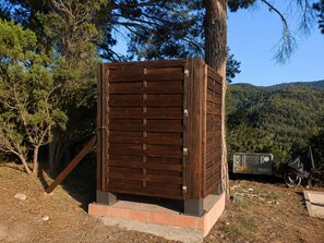 A wooden structure with a metal door, surrounded by trees and a hilly landscape. - Camera tripla del Geco natura e relax (Marciana)