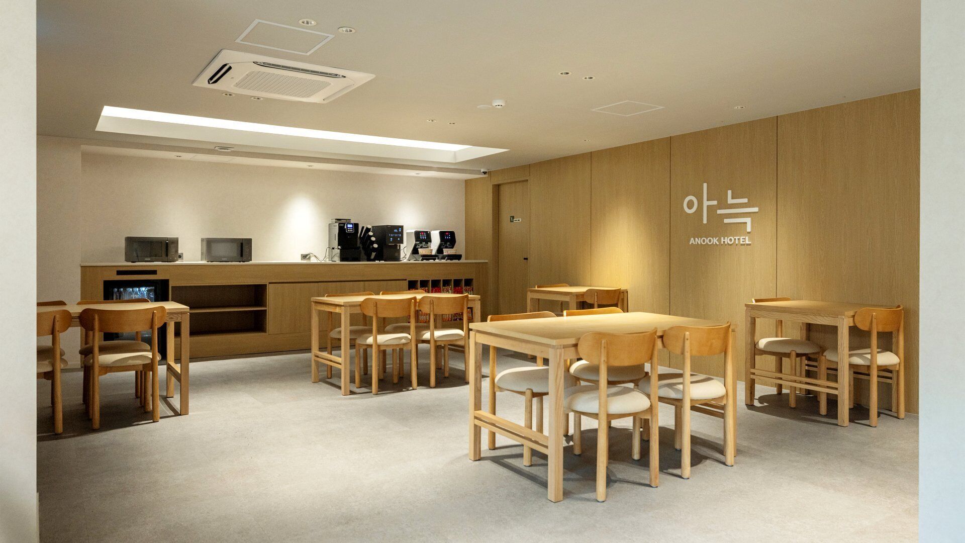 A hotel room with wooden furniture, a kitchenette, and a ceiling with recessed lighting.