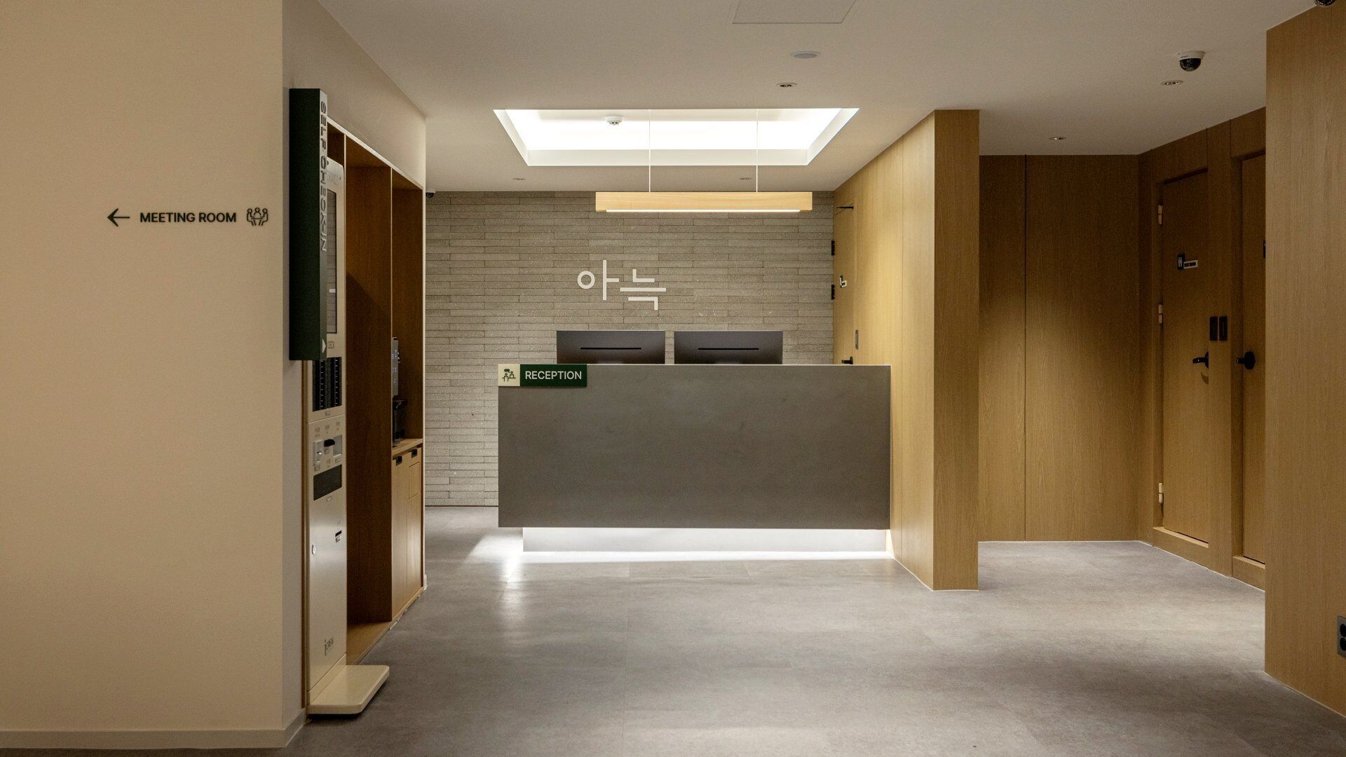 Un mostrador de recepción con un letrero de recepción, un letrero para sala de reuniones y un área de recepción con tragaluces.