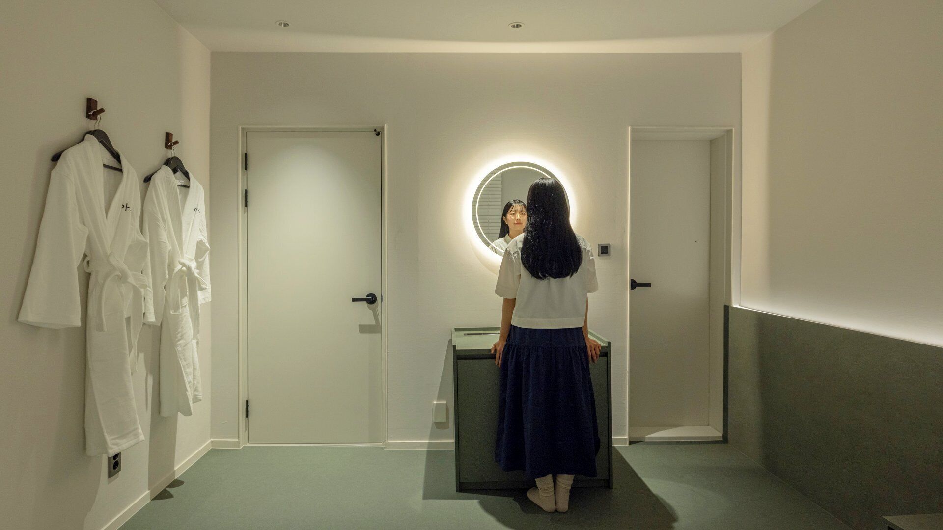A hallway with a mirror, a door, and a rack of white robes.