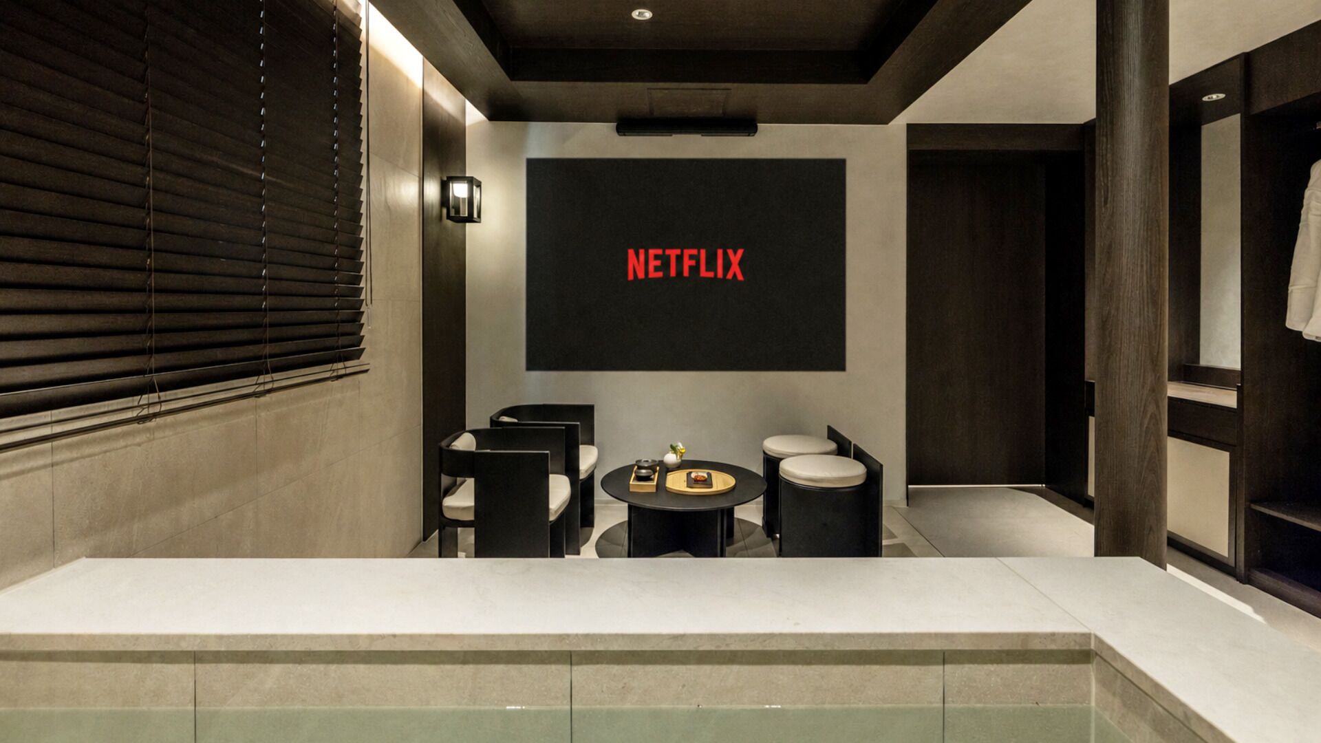 Un baño moderno con un espejo grande, un lavabo y una pantalla en la pared que muestra 'NETFLIX'.