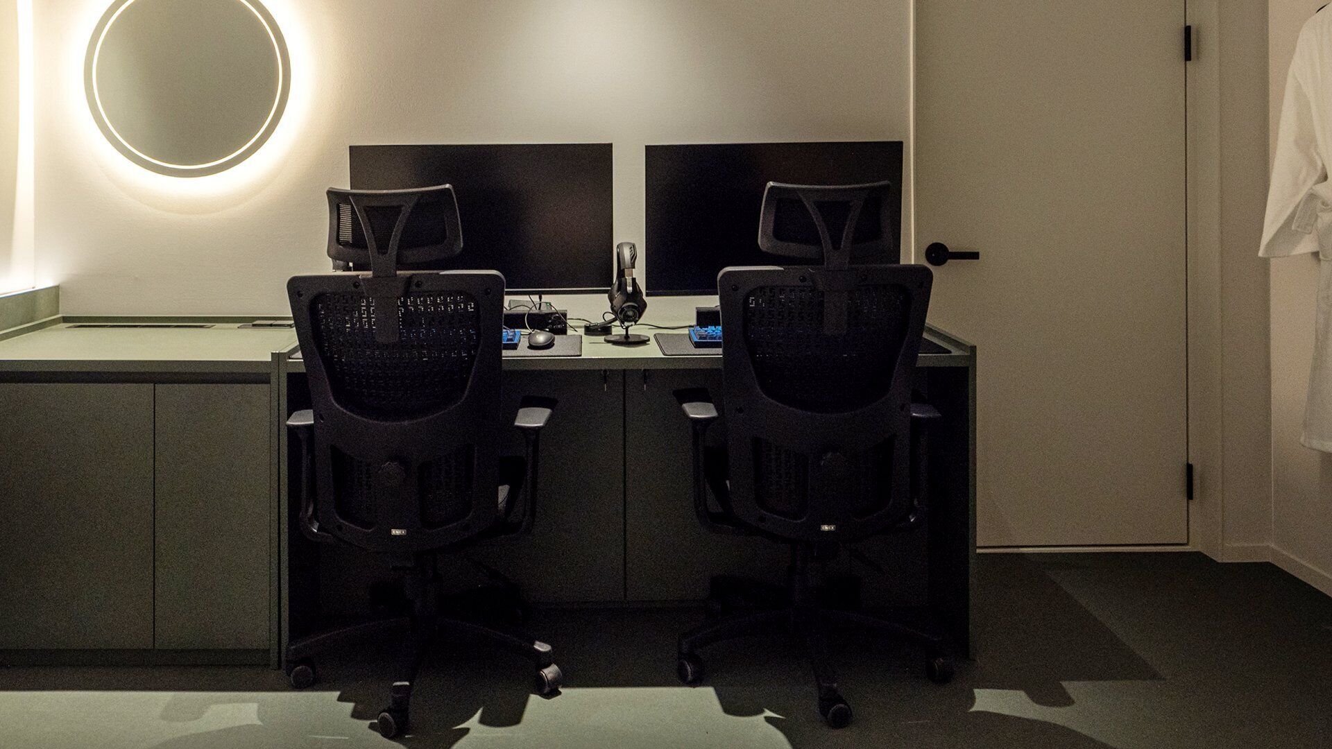 A hotel room with a desk, two chairs, a computer, and a mirror.