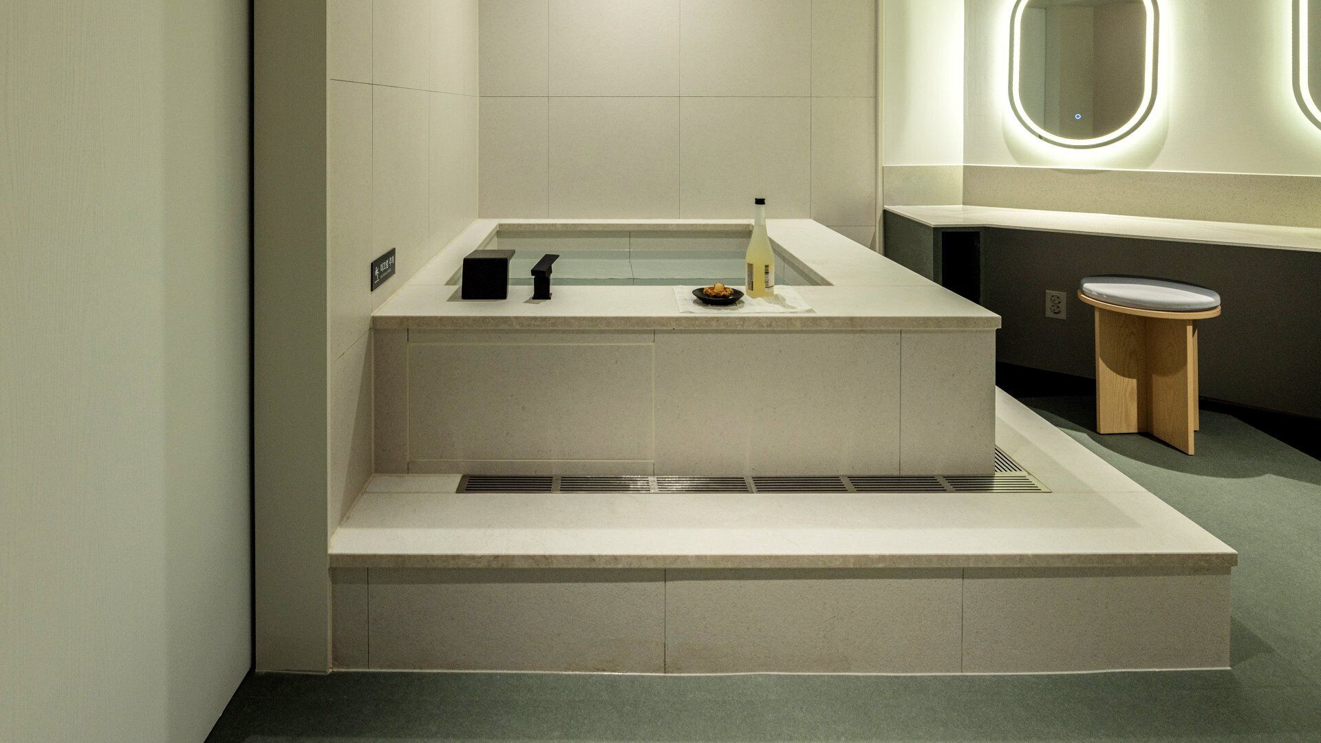 A modern bathroom with a built-in bathtub, a small sink, and a wooden stool.