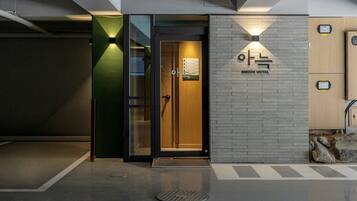 A hotel entrance with a glass door, a signboard with room numbers, and a brick wall with the hotel name.
