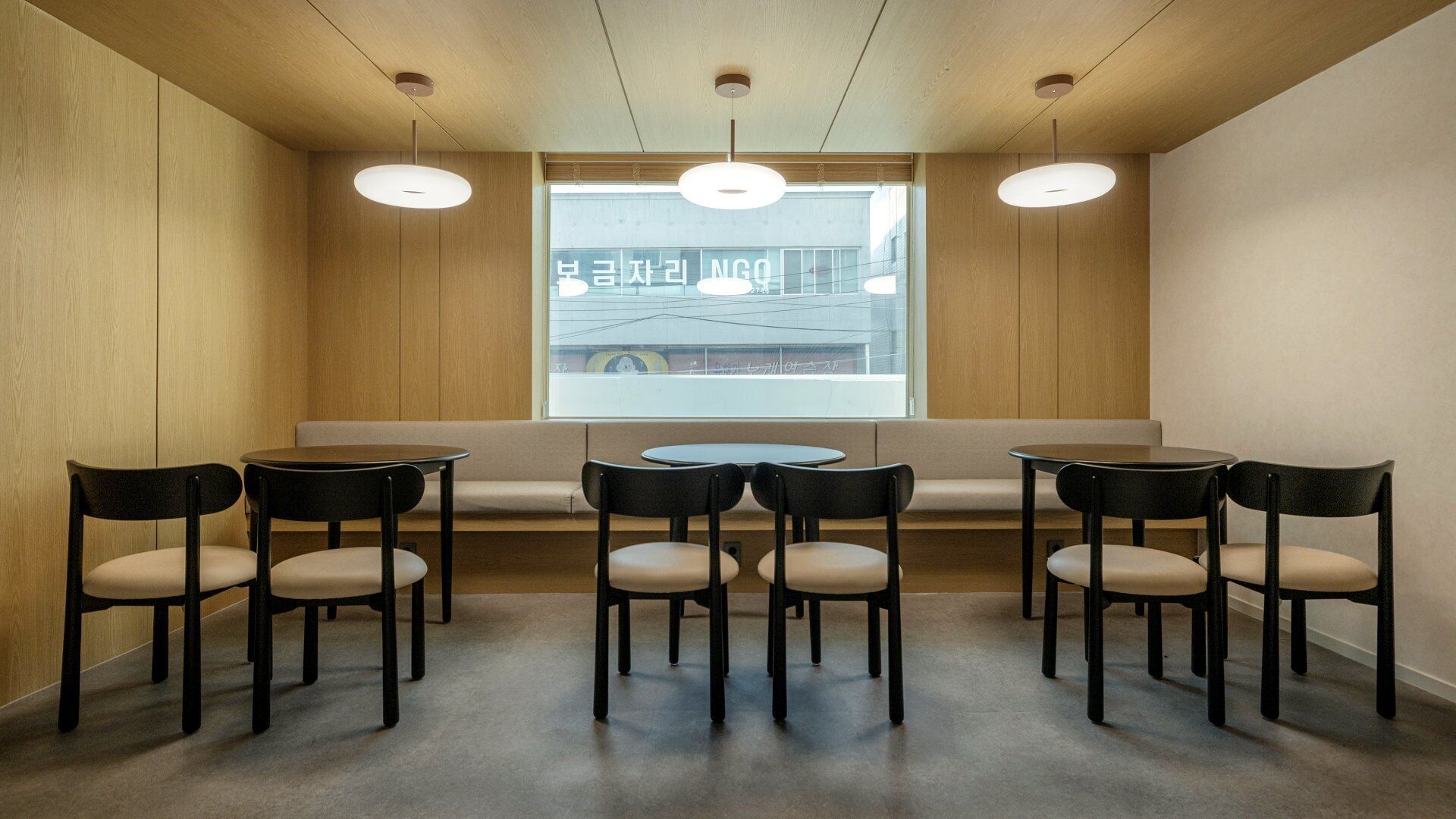 A conference room with a long table, six chairs, a bench, and three pendant lights.