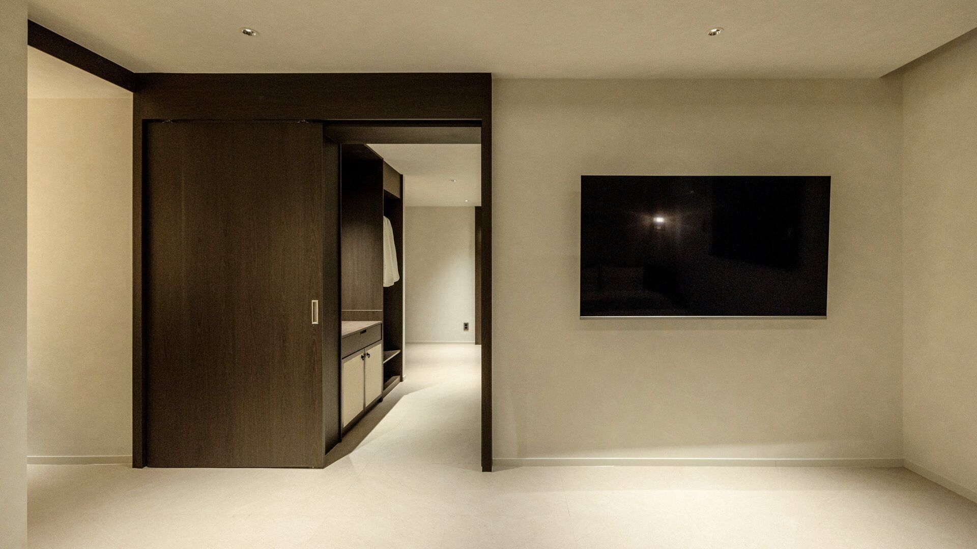 Un interior moderno con un pasillo que conduce a una habitación, una obra de arte oscura colgada en la pared y un armario de madera.