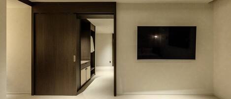 A modern interior with a hallway leading to a room, a dark wall-mounted artwork, and a wooden wardrobe.