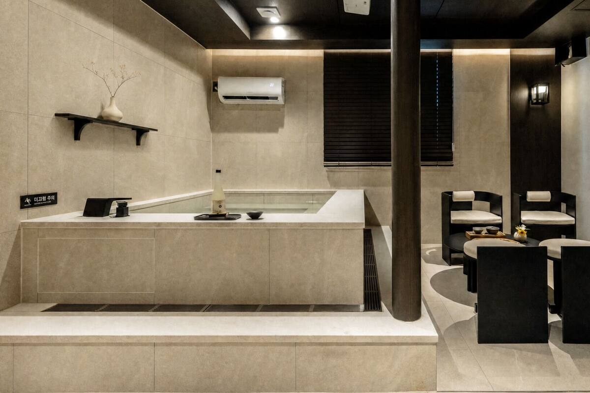 Une salle de bain moderne avec une grande baignoire, un petit lavabo et des toilettes. On y trouve une étagère avec un vase et un panneau.
