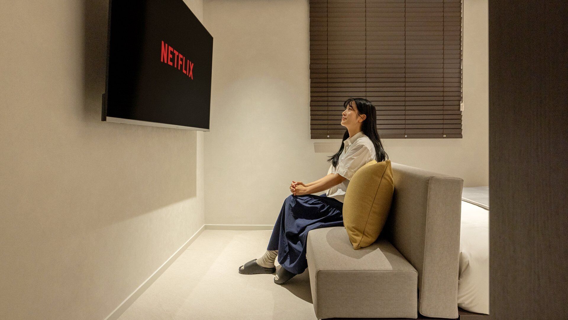 A person sitting on a couch in a room with a wall-mounted TV displaying the Netflix logo.