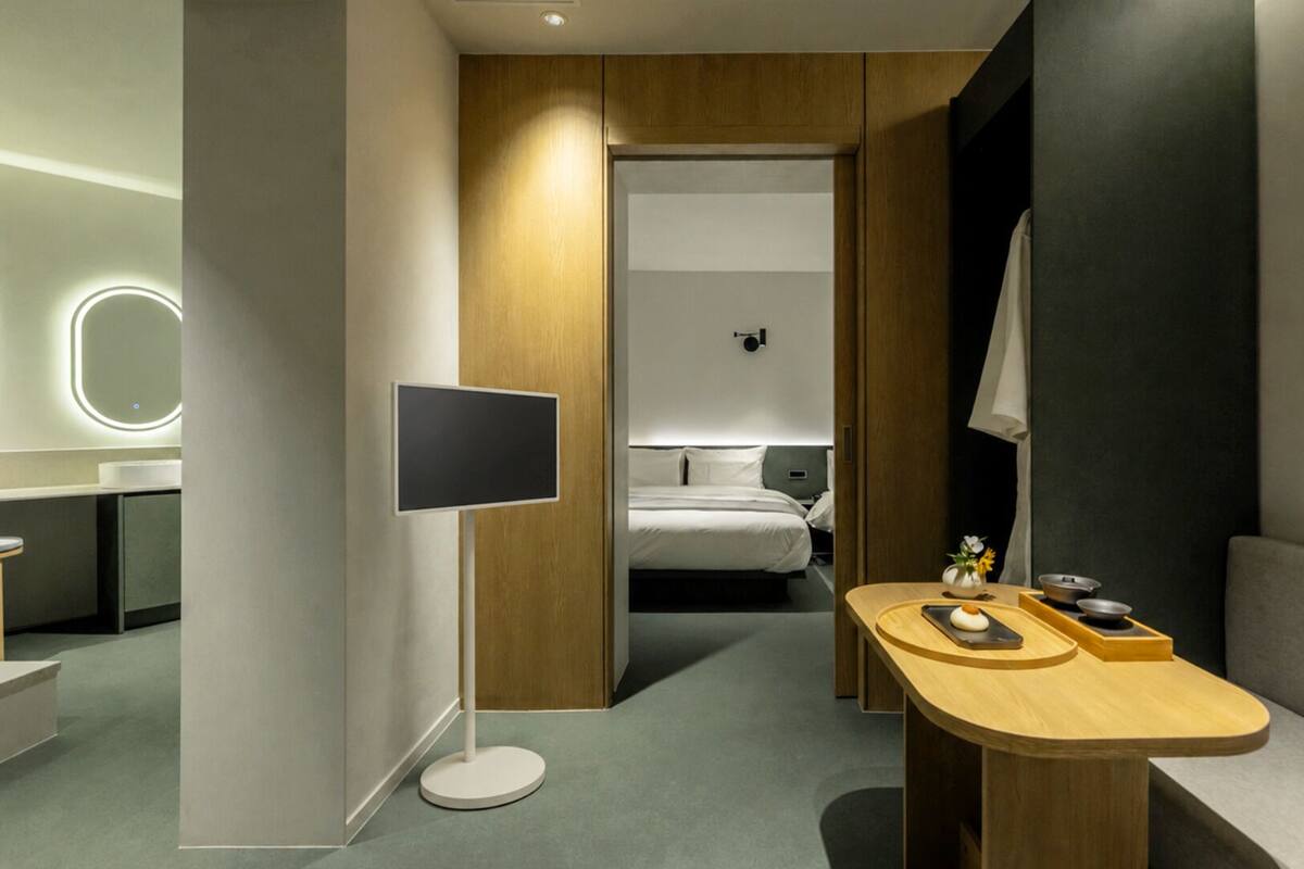 Une chambre d’hôtel moderne équipée d’un lit, d’un bureau, d’un téléviseur à écran plat et d’une petite table agrémentée d’un vase et d’un bol.