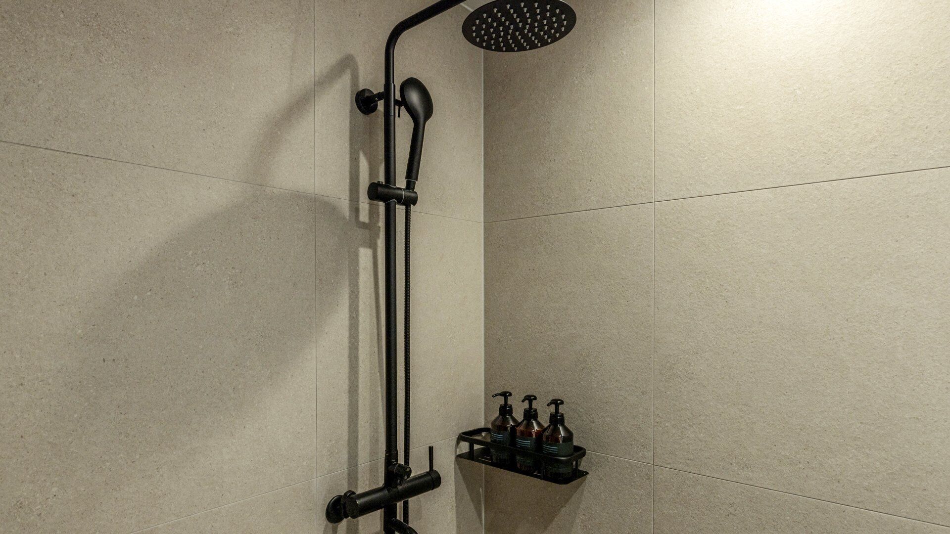 A shower with a handheld head, a wall-mounted shelf with toiletries, and tiled walls.