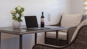 En bærbar computer på et bord sammen med en vinflaske og et glas, en vase med blomster og en fletstol.