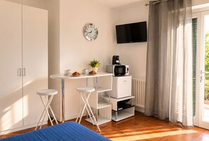 Ein kleines Zimmer mit Küchenzeile, Flachbildfernseher, einer Uhr und einer Schiebetür zum Außenbereich.