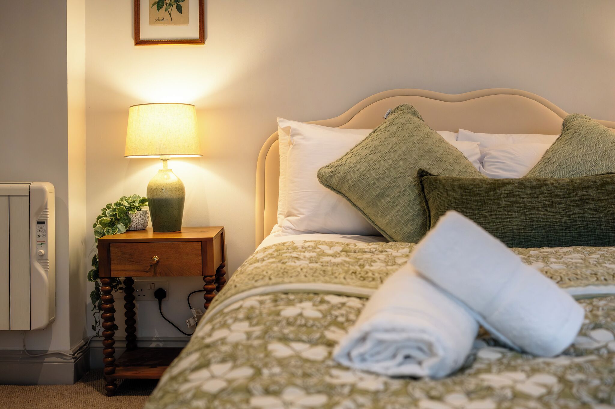 A neatly made bed with a patterned bedspread, a lamp on a bedside table, and a wall-mounted picture.