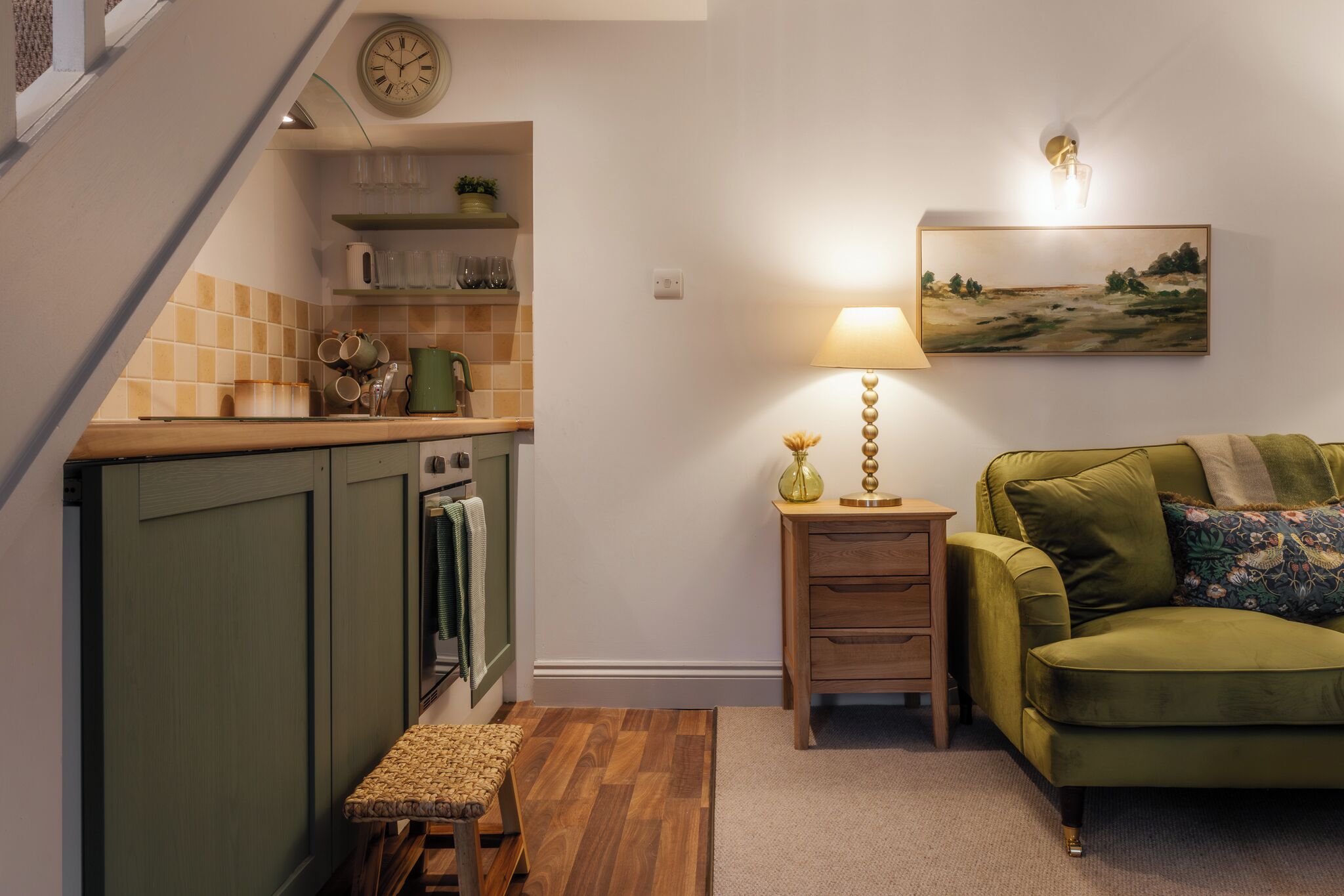 A compact living space with a kitchen, a green sofa, a lamp, and a painting on the wall.