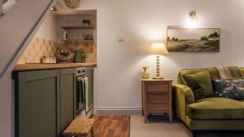 A compact living space with a kitchen, a green sofa, a lamp, and a painting on the wall.