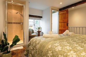 A bedroom with a large bed, a shower, a wooden door, and a window with a view. - Little Cottage in Moreton-in-Marsh (Moreton-in-Marsh)