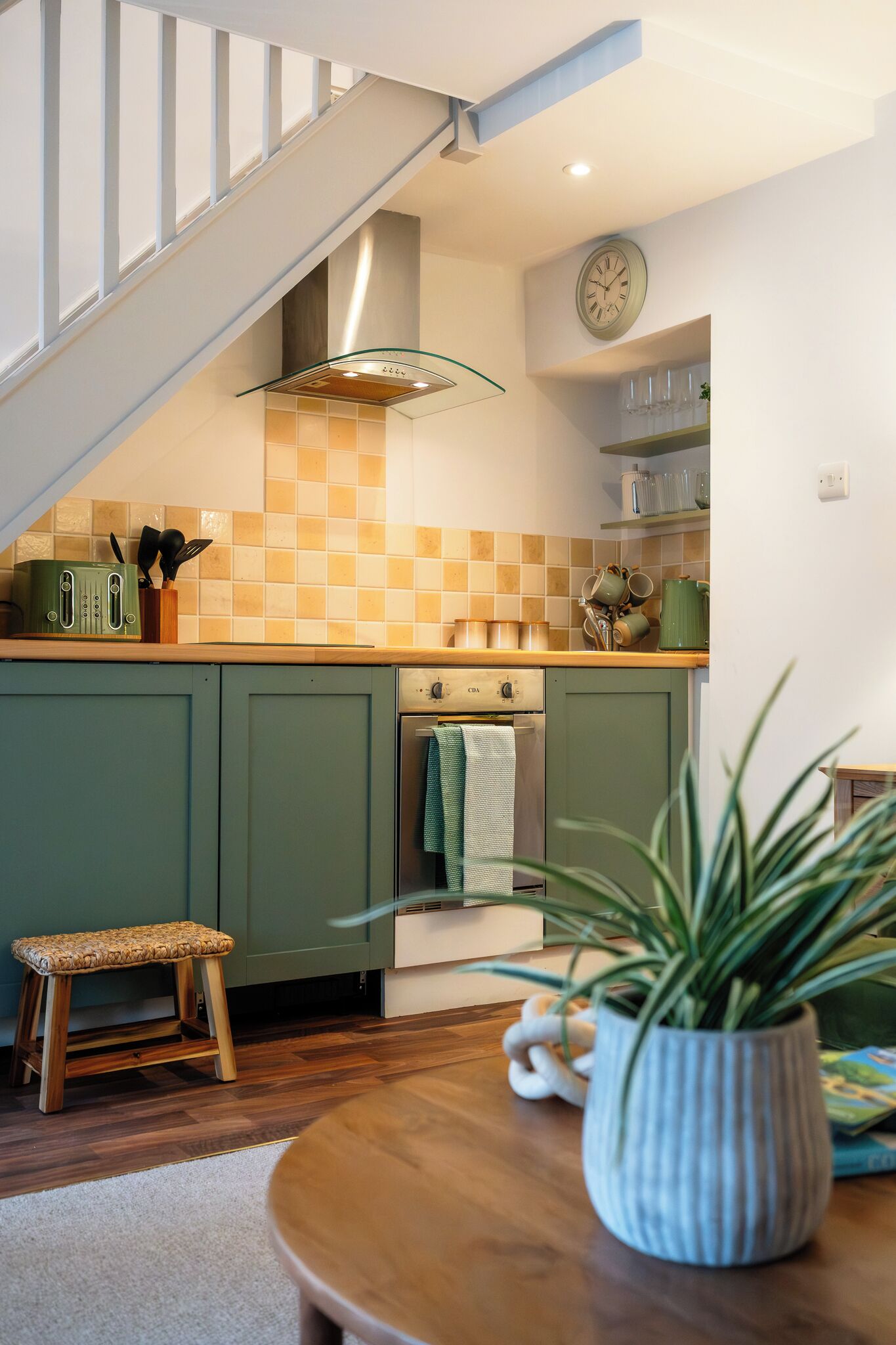 A kitchen with green cabinets, a wooden bench, a potted plant, and a staircase.