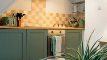 A kitchen with green cabinets, a wooden bench, a potted plant, and a staircase.