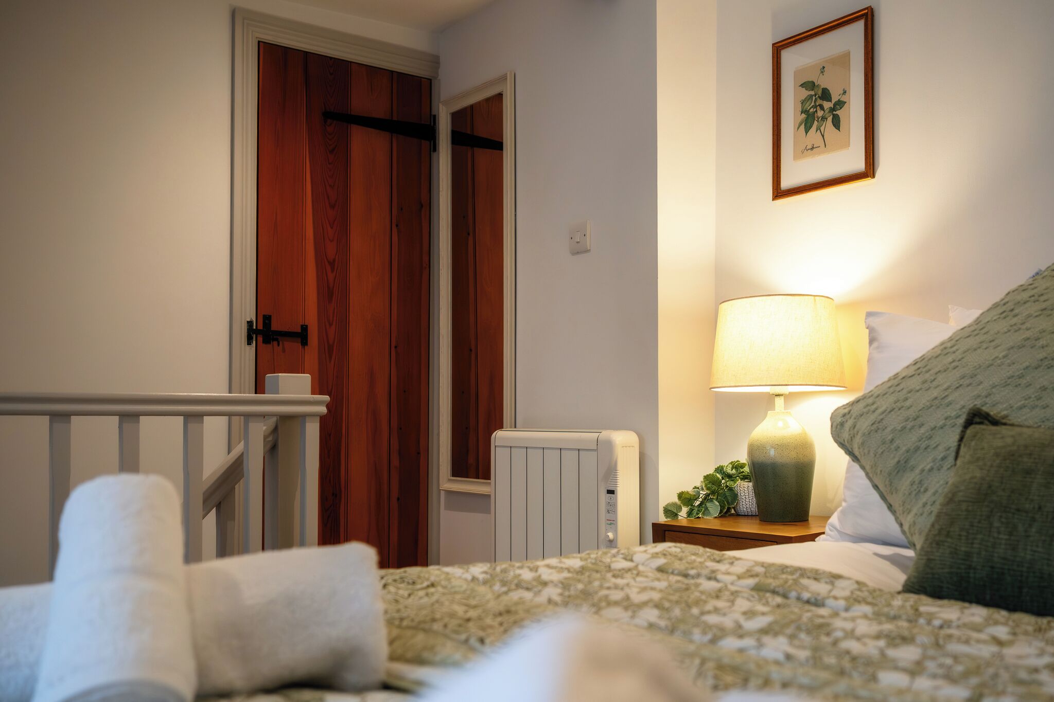 Un dormitorio con una cama, una mesita de noche con lámpara, un radiador y una puerta.