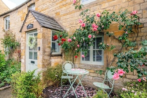 A stone building with a door, a window, and a small garden area with chairs and a table. - Little Cottage in Moreton-in-Marsh (Moreton-in-Marsh)