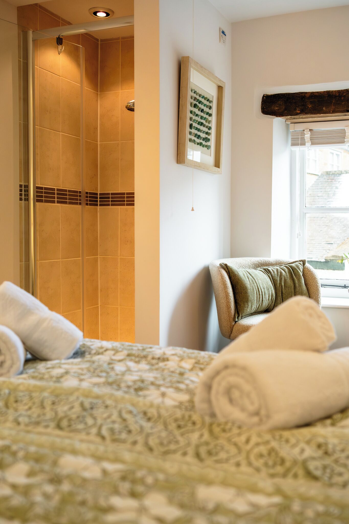 A hotel room with a bed, a chair, a shower, and a window.