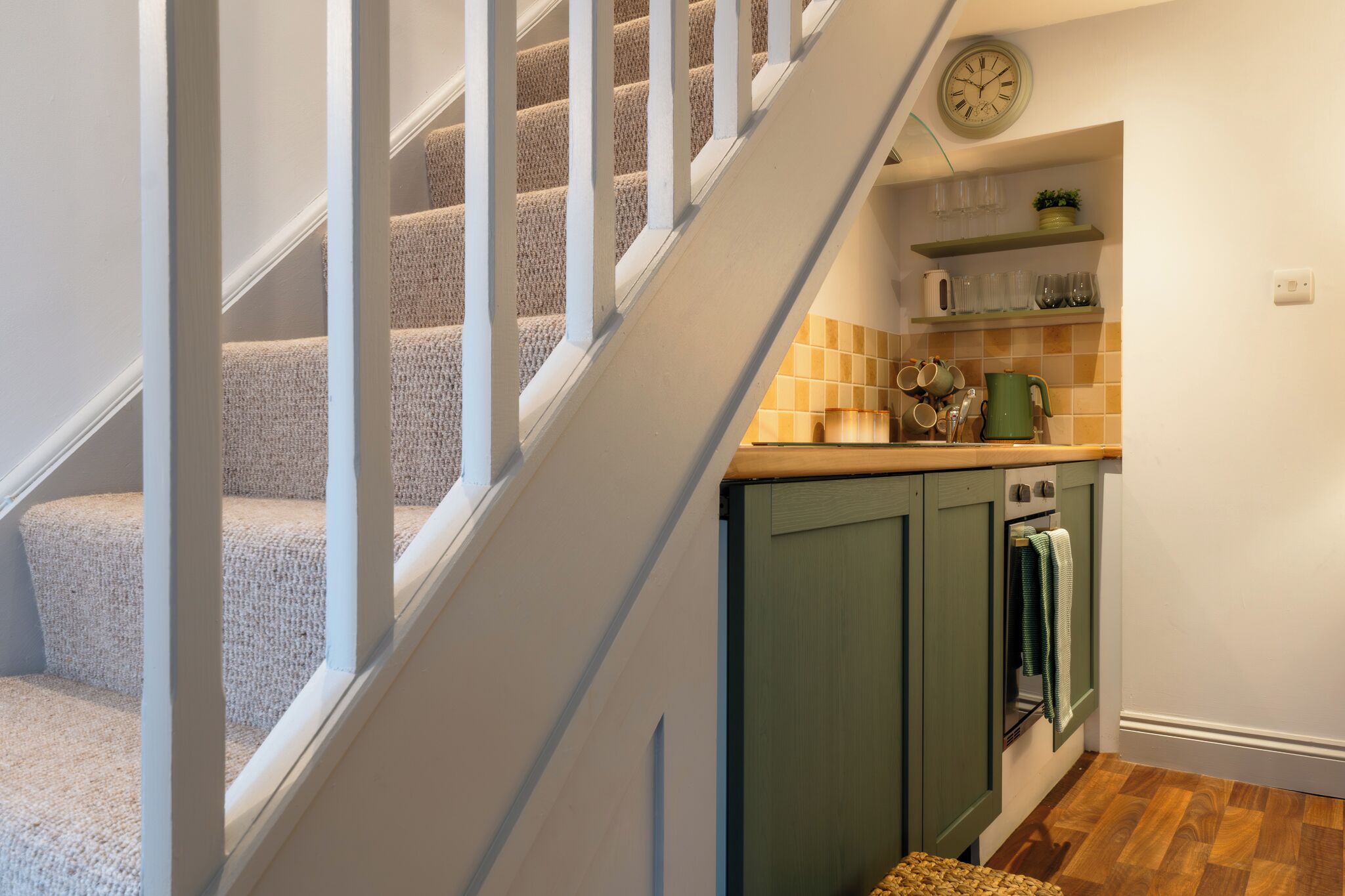 A staircase leading to a kitchen with green cabinets, a stove, and a clock on the wall.