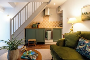 A kitchen with a staircase, a green sofa, a lamp, and a plant. - Little Cottage in Moreton-in-Marsh (Moreton-in-Marsh)
