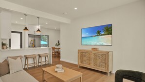 A modern living room with a wooden coffee table, a sofa, and a TV displaying a beach scene. - Airport Casita •FULL PRIVACY• 5min Airport •2min Walk to IHOP• remodeled 2026 (Miami Springs)