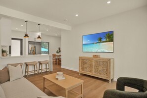 Ein modernes Wohnzimmer mit Couch, Fernseher und Couchtisch aus Holz. Auf dem Fernseher ist eine Strandansicht zu sehen.