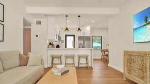 A modern living room with a sofa, a wooden coffee table, and a kitchen in the background. - Airport Casita •FULL PRIVACY• 5min Airport •2min Walk to IHOP• remodeled 2026 (Miami Springs)