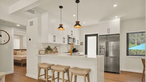 A modern kitchen with white cabinets, a stainless steel refrigerator, and a bar area with stools. - Airport Casita •FULL PRIVACY• 5min Airport •2min Walk to IHOP• remodeled 2026 (Miami Springs)