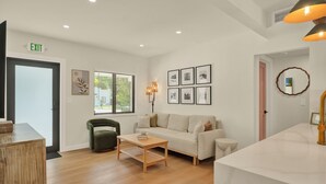 A modern hotel room with a wooden floor, a sofa, a small table, and a large window with blinds. - Airport Casita •FULL PRIVACY• 5min Airport •2min Walk to IHOP• remodeled 2026 (Miami Springs)