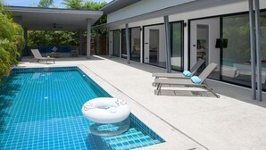 A modern outdoor pool area with a covered patio, lounge chairs, and a floating ring. - Wantana villa Sawaree villa 1 V308 (Chang Wat Surat Thani)