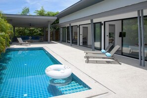 A modern outdoor pool area with a covered patio, lounge chairs, and a floating ring. - Wantana villa Sawaree villa 1 V308 (Chang Wat Surat Thani)