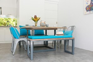 Ein Essbereich mit Holztisch und Bänken, einer Blumenvase und einem farbenfrohen abstrakten Gemälde an der Wand.