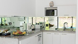 A modern kitchen with white cabinetry, a granite countertop, a microwave, and a fruit bowl. - Wantana villa Sawaree villa 1 V308 (Chang Wat Surat Thani)